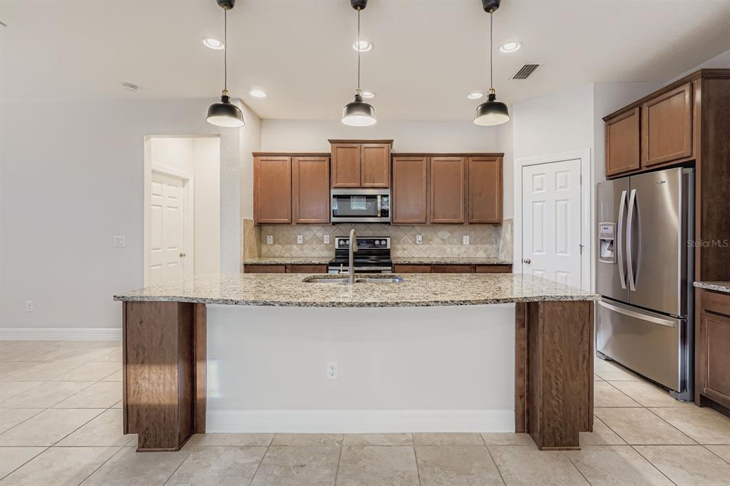 16355 Treasure Point Drive Wimauma, FL 33598 - Photo 11 of 28 a kitchen with stainless steel appliances granite countertop a sink a stove a refrigerator and island