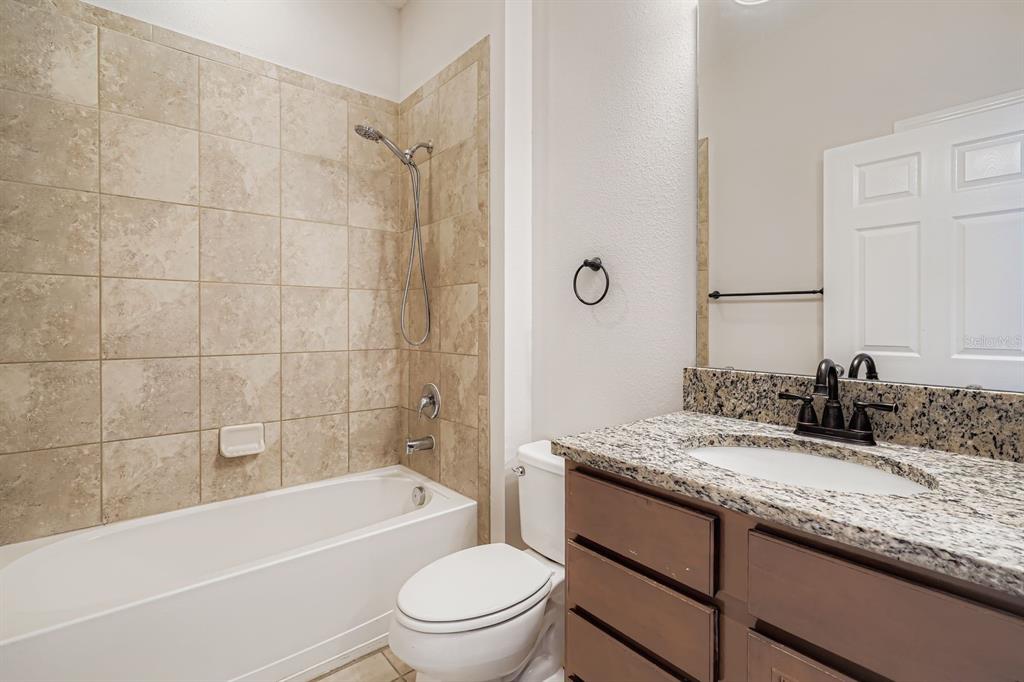 16355 Treasure Point Drive Wimauma, FL 33598 - Photo 26 of 28 a bathroom with a granite countertop toilet a sink and bathtub