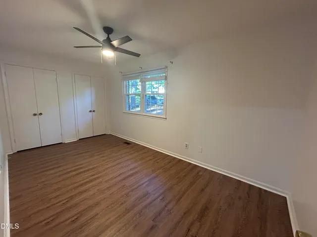 an empty room with wooden floor chandelier fan and windows