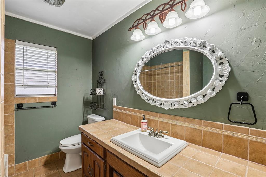 1600 South Timber Court Benbrook, TX 76126 - Photo 17 of 30 Bathroom vanity with tile countertop and integrated sink, framed by an ornate oval mirror