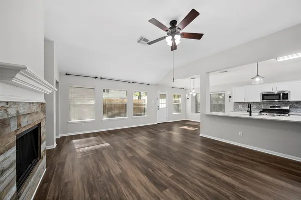 a kitchen with stainless steel appliances granite countertop a stove a sink dishwasher a refrigerator white cabinets and wooden floor next to a window