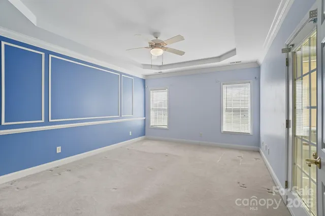 an empty room with chandelier fan and windows