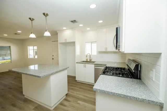 a kitchen with kitchen island granite countertop a stove a sink a refrigerator and white cabinets with wooden floor