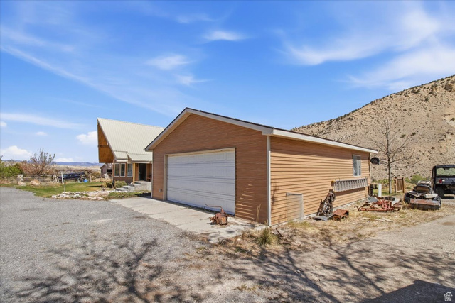 811 East Canyon Road Mayfield, UT 84643 - Photo 39 of 57 Detached garage with a white overhead door and tan siding, featuring a concrete driveway and gravel parking area