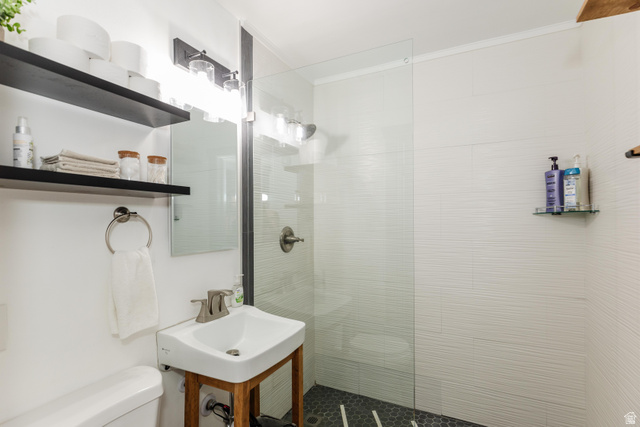 130 North 100 East Logan, UT 84321 - Photo 14 of 35 Contemporary bathroom featuring a glass-enclosed shower with textured wall tile, a single vanity with a white basin, matte black wall-mounted shelving, and recessed lighting