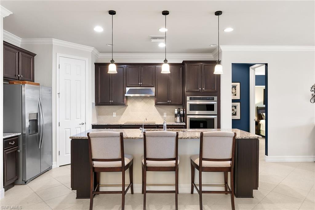 8407 Benelli Court Naples, FL 34114 - Photo 13 of 50 a kitchen with stainless steel appliances granite countertop a kitchen island a stove a refrigerator a oven a sink with a dining table and chairs
