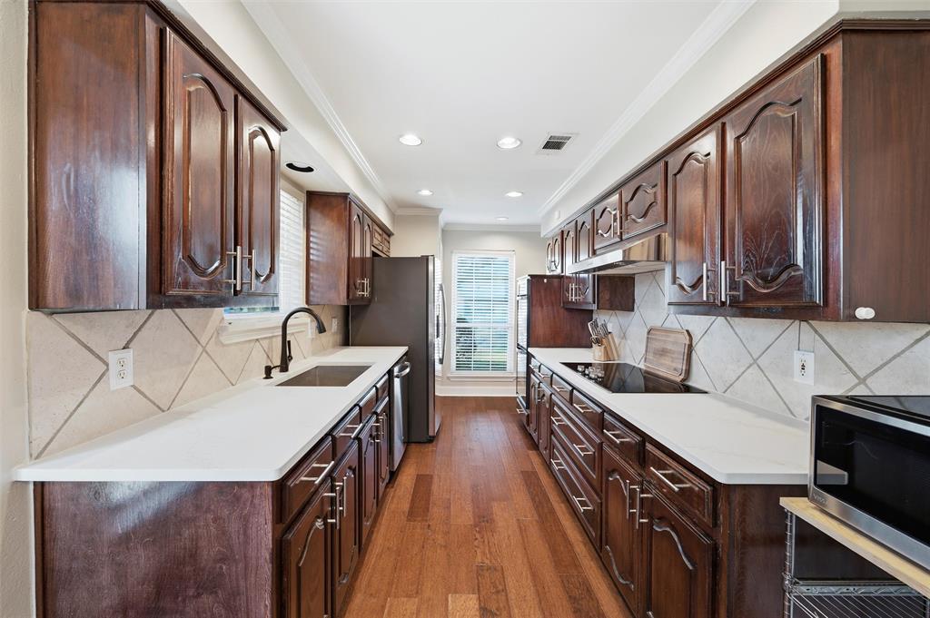 1704 Throwbridge Lane Plano, TX 75023 - Photo 19 of 40 Kitchen features smooth ceiling with crown molding and recessed lighting. Cabinetry extends to the ceiling, paired with quartz countertops and tile backsplash. Appliances include dual electric ovens, electric cooktop, and dishwasher. Pantry provides additional storage, with hardwood flooring extending throughout and direct connection to adjacent breakfast area.