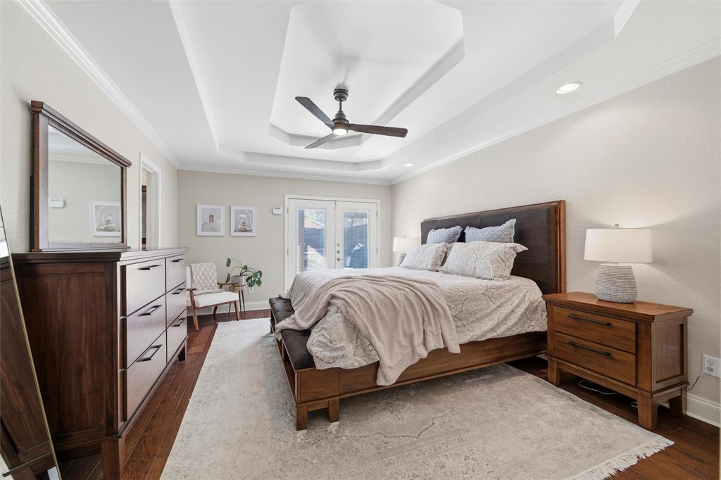 1704 Throwbridge Lane Plano, TX 75023 - Photo 20 of 40 Primary bedroom features tray ceiling with crown molding, recessed lighting, and a ceiling-mounted fan. Double glass-panel doors provide exterior access, with direct entry to the en-suite bathroom and hardwood flooring extending throughout the space.