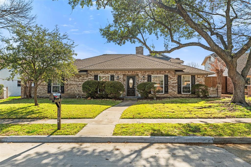 1704 Throwbridge Lane Plano, TX 75023 - Photo 2 of 40 Front exterior features traditional brick construction, multiple front-facing windows with decorative shutters, and a centered front entry. A straight concrete walkway leads from the sidewalk to the front door, bordered by maintained lawn, trimmed shrubs, and mature trees providing natural shade.