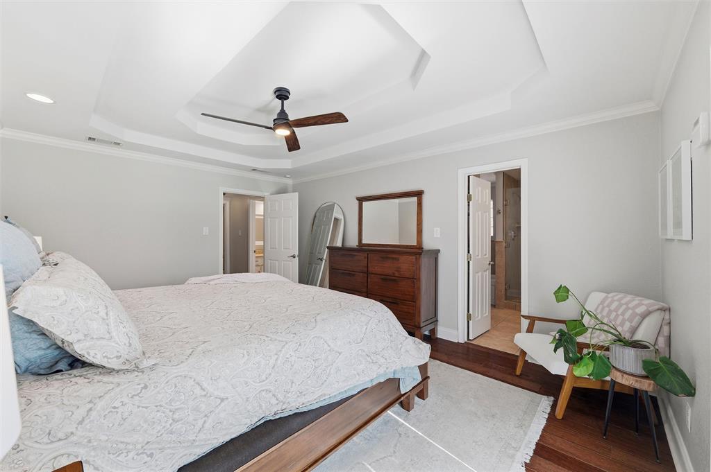 1704 Throwbridge Lane Plano, TX 75023 - Photo 21 of 40 Primary bedroom features tray ceiling with crown molding, recessed lighting, and a ceiling-mounted fan. Double glass-panel doors provide exterior access, with direct entry to the en-suite bathroom and hardwood flooring extending throughout the space.