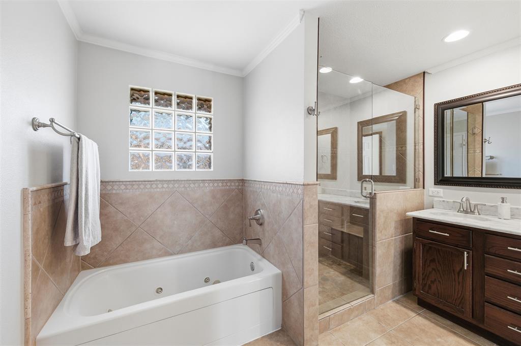 1704 Throwbridge Lane Plano, TX 75023 - Photo 22 of 40 Primary bathroom features smooth ceiling with recessed lighting. Glass-enclosed walk-in shower and separate soaking tub are finished with tile surrounds. Dual-sink vanity includes a continuous vanity countertop and framed mirrors, with tile flooring throughout the space.