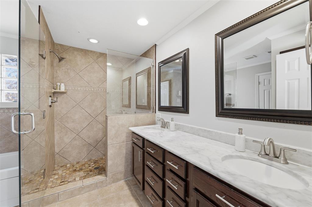 1704 Throwbridge Lane Plano, TX 75023 - Photo 23 of 40 Primary bathroom features smooth ceiling with recessed lighting. Glass-enclosed walk-in shower and separate soaking tub are finished with tile surrounds. Dual-sink vanity includes a continuous vanity countertop and framed mirrors, with tile flooring throughout the space.