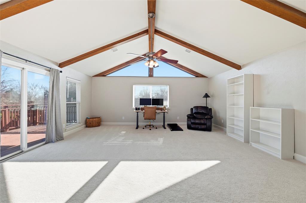 1704 Throwbridge Lane Plano, TX 75023 - Photo 27 of 40 Game Room features vaulted ceiling with exposed wood beams and ceiling fan with integrated light. Brick fireplace with raised hearth includes a gas starter, complemented by large windows and a sliding glass door providing natural light and exterior access. Carpet flooring extends throughout.