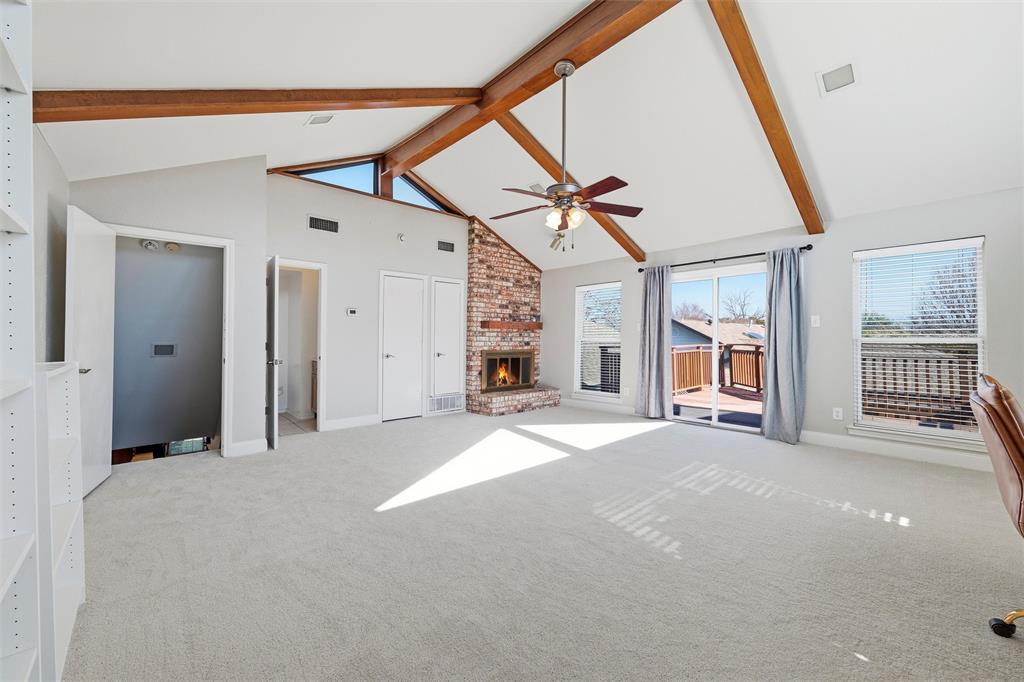 1704 Throwbridge Lane Plano, TX 75023 - Photo 28 of 40 Game Room features vaulted ceiling with exposed wood beams and ceiling fan with integrated light. Brick fireplace with raised hearth includes a gas starter, complemented by large windows and a sliding glass door providing natural light and exterior access. Carpet flooring extends throughout.