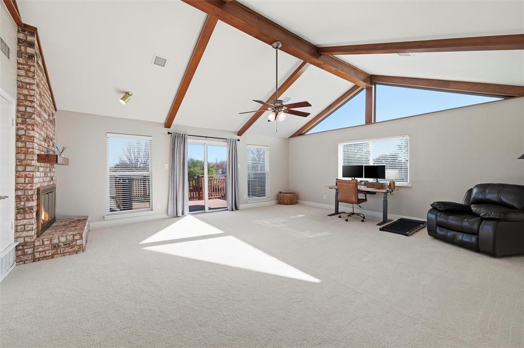 1704 Throwbridge Lane Plano, TX 75023 - Photo 29 of 40 Game Room features vaulted ceiling with exposed wood beams and ceiling fan with integrated light. Brick fireplace with raised hearth includes a gas starter, complemented by large windows and a sliding glass door providing natural light and exterior access. Carpet flooring extends throughout.