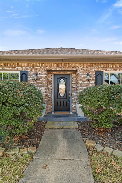 1704 Throwbridge Lane Plano, TX 75023 - Photo 3 of 40 Front exterior features traditional brick construction, multiple front-facing windows with decorative shutters, and a centered front entry. A straight concrete walkway leads from the sidewalk to the front door, bordered by maintained lawn, trimmed shrubs, and mature trees providing natural shade.