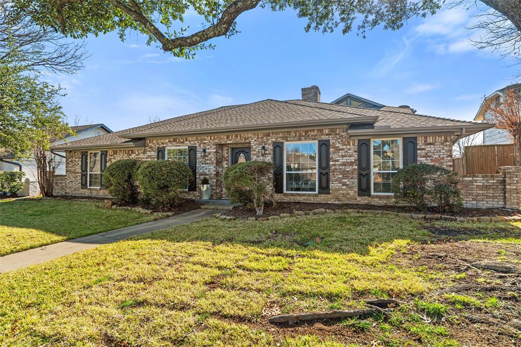 1704 Throwbridge Lane Plano, TX 75023 - Photo 5 of 40 Front exterior features traditional brick construction, multiple front-facing windows with decorative shutters, and a centered front entry. A straight concrete walkway leads from the sidewalk to the front door, bordered by maintained lawn, trimmed shrubs, and mature trees providing natural shade.