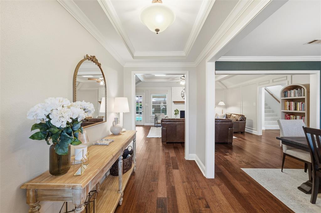 1704 Throwbridge Lane Plano, TX 75023 - Photo 7 of 40 Entry hallway features tray ceiling with crown molding and a ceiling-mounted light fixture. Wide cased openings connect the space to adjacent living areas, with hardwood flooring continuing throughout.