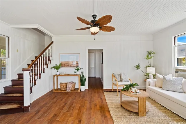 a living room with couches a dining table and a chandelier with wooden floor