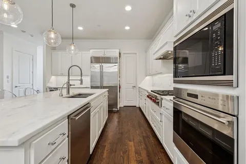 a white kitchen with stainless steel appliances granite countertop a stove and a sink