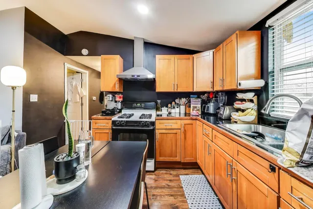 a kitchen with stainless steel appliances granite countertop a refrigerator a sink dishwasher a stove and a dining table with wooden floor