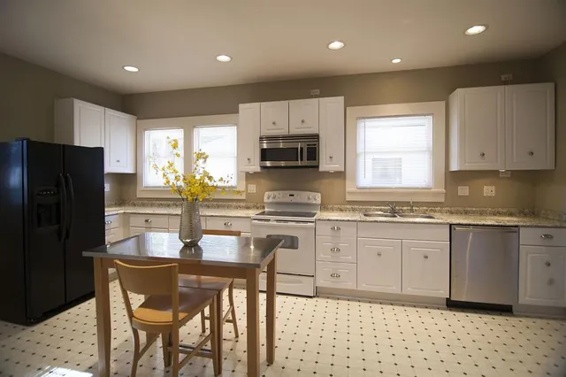 a kitchen with granite countertop white cabinets a refrigerator a stove a microwave and island with wooden floor