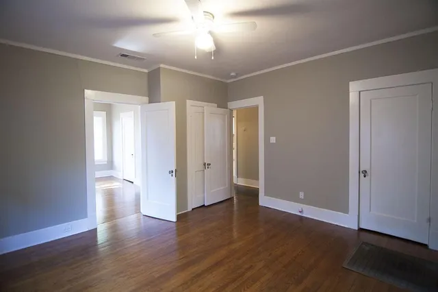a view of an empty room with wooden floor and a ceiling fan