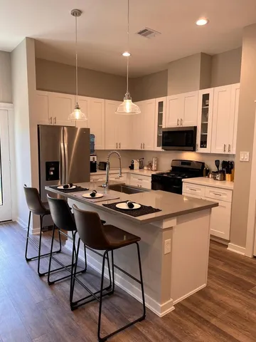 a kitchen with stainless steel appliances granite countertop a stove top oven a refrigerator a sink and white cabinets with wooden floor