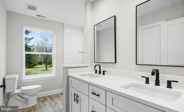 a bathroom with a toilet a sink a mirror a window and vanity