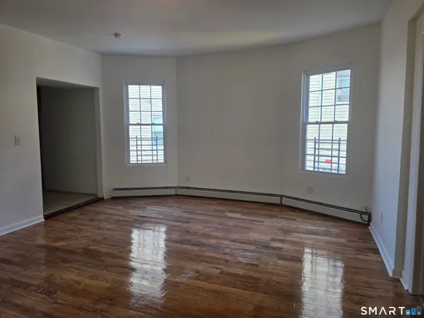 a view of an empty room with wooden floor and a window