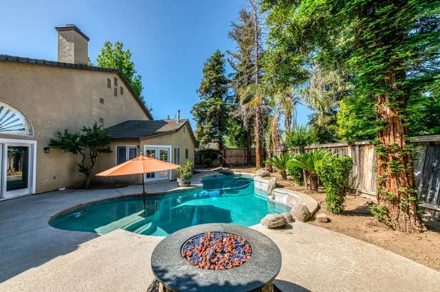 a backyard of a house with table and chairs potted plants and large tree