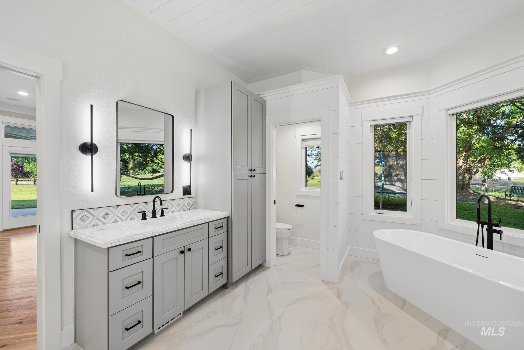 2050 Artesian Road Eagle, ID 83616 - Photo 28 of 49 Contemporary bathroom featuring a freestanding soaking tub with a matte black floor-mounted faucet, a walk-in shower with a rain shower head and glass enclosure, dual vanity sinks with light gray cabinetry and white countertops, and shiplap wall accents