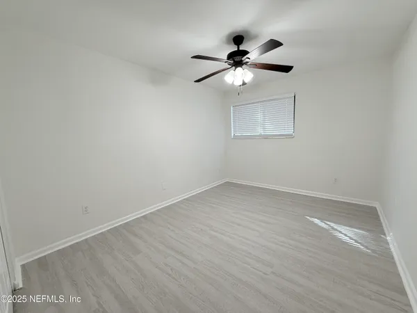 an empty room with wooden floor fan and windows