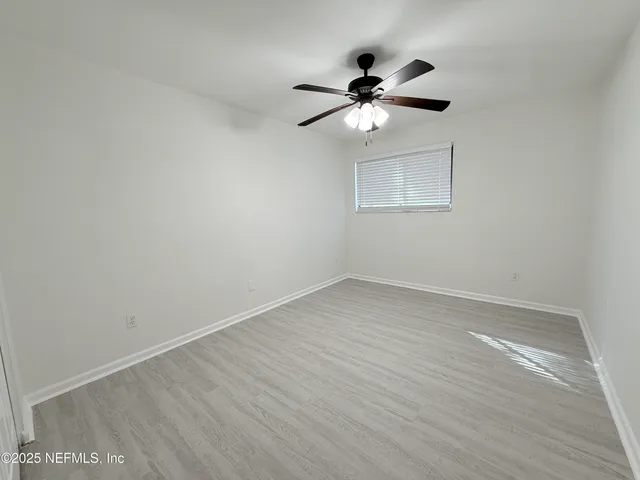 an empty room with wooden floor fan and windows