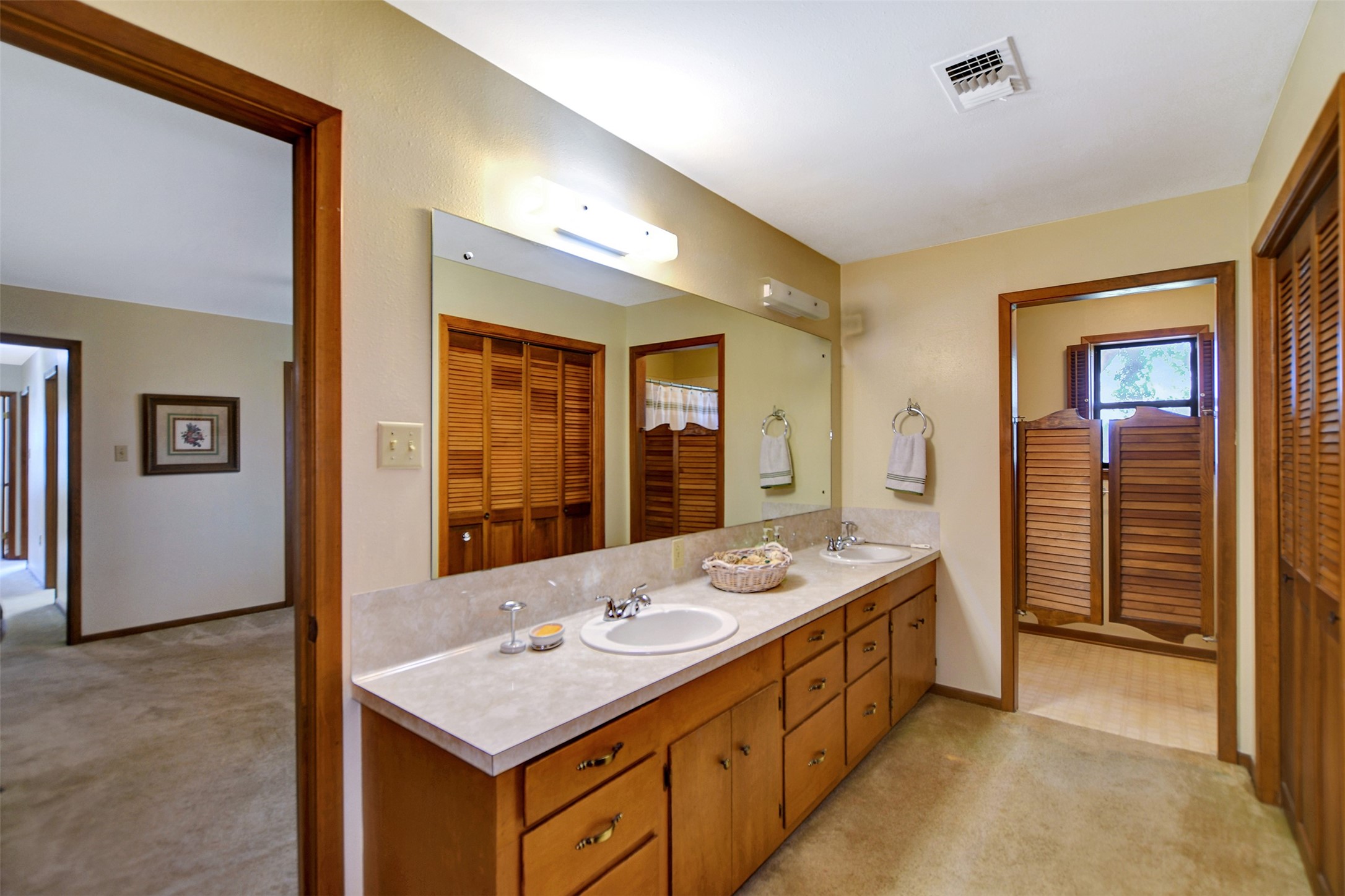 341 South S Loop Bellville, TX 77418 - Photo 23 of 33 This spacious bathroom features a long vanity with dual sinks, ample cabinet storage, and a large mirror. It connects to a hallway and has a separate area with shutter doors for privacy. The room is warmly lit, complementing the wood accents.