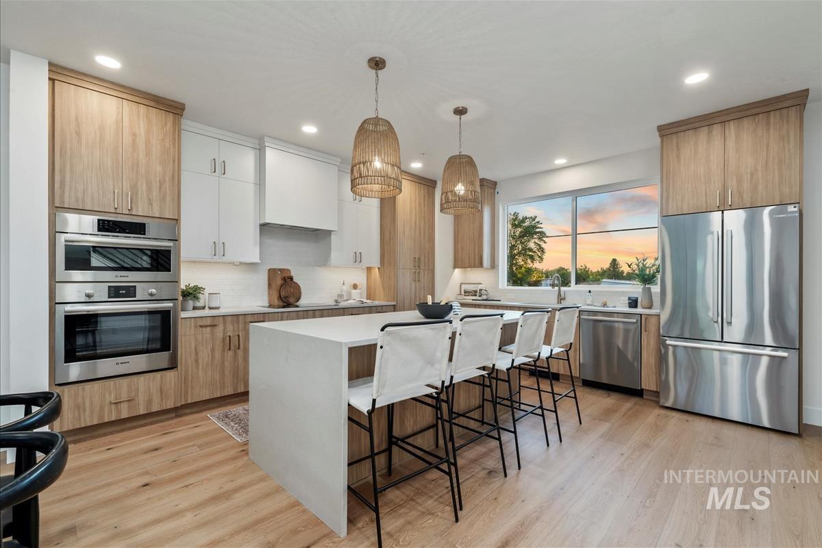 3219 West Moore Street Boise, ID 83702 - Photo 11 of 34 Kitchen with appliances with stainless steel finishes, a breakfast bar, light brown cabinetry, decorative light fixtures, and light wood finished floors