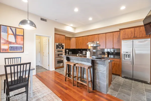 a kitchen with stainless steel appliances granite countertop a refrigerator a stove a sink a dining table and chairs with wooden floor
