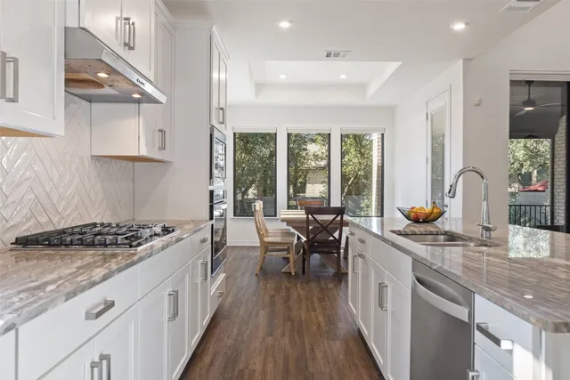 a kitchen with stainless steel appliances granite countertop a stove a sink dishwasher a refrigerator and a dining table with wooden floor