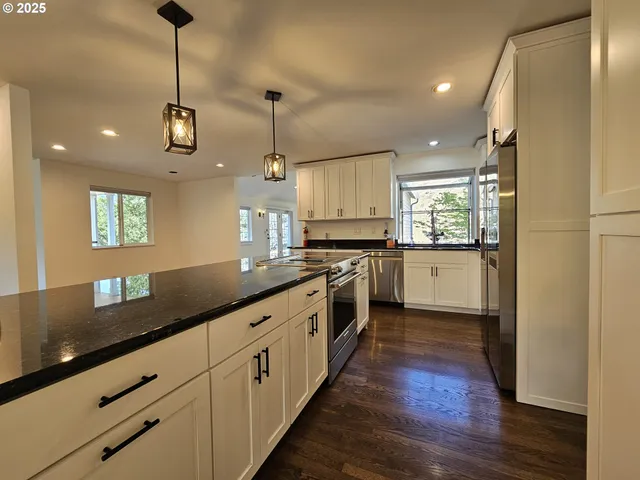 a large kitchen with granite countertop a large counter top space a sink stainless steel appliances and cabinets
