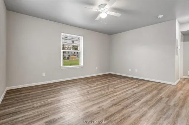 an empty room with wooden floor chandelier fan and windows