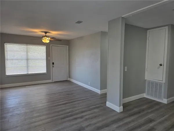 an empty room with wooden floor chandelier fan and windows