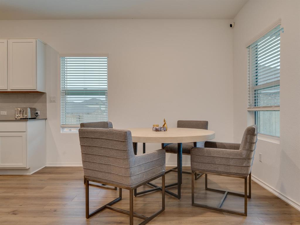 1208 Sweetspire Street Leander, TX 78641 - Photo 9 of 36 Open-concept dining area featuring wood-finish flooring, white cabinetry, a light gray subway tile backsplash, and two windows with blinds