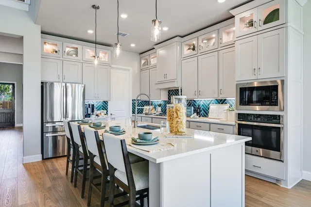 a kitchen with stainless steel appliances kitchen island granite countertop a stove a refrigerator a oven a white table and chairs with wooden floor