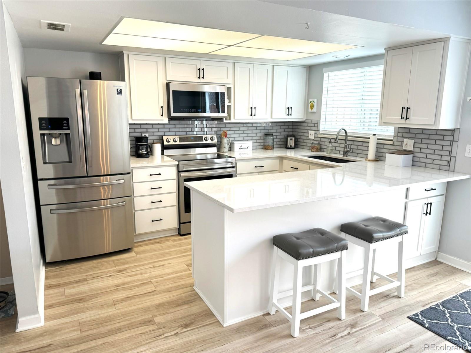a kitchen with stainless steel appliances a stove a sink refrigerator and white cabinets with wooden floor