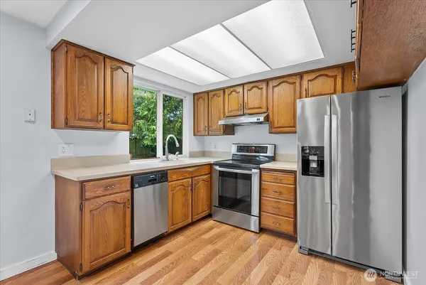a kitchen with stainless steel appliances granite countertop a refrigerator a sink dishwasher a stove and white countertops with wooden floor