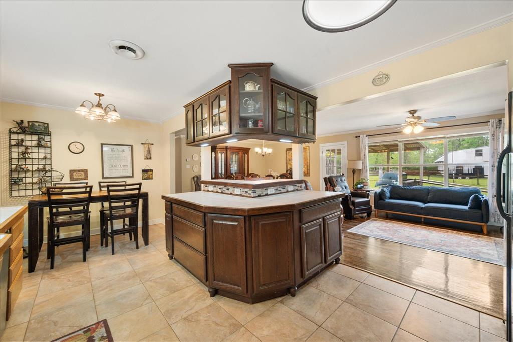 14036 Old Texaco Road Conroe, TX 77302 - Photo 8 of 40 Kitchen featuring crown molding, dark brown cabinets, glass insert cabinets, ceiling fan with notable chandelier, and light tile patterned floors