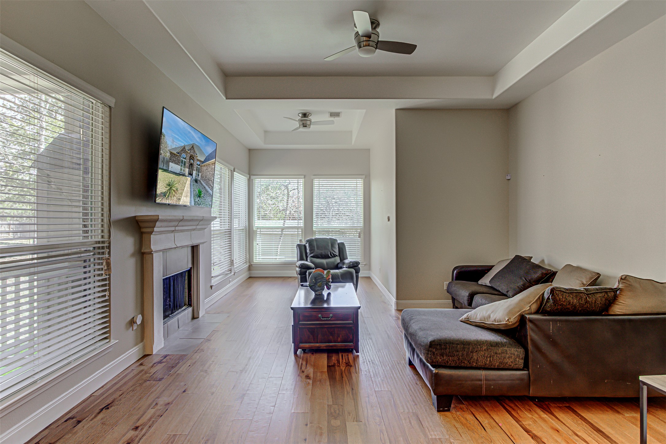 105 Arbors Circle Elgin, TX 78621 - Photo 19 of 40 Living room with a tray ceiling, ceiling fan, light wood-style flooring, and a fireplace with flush hearth