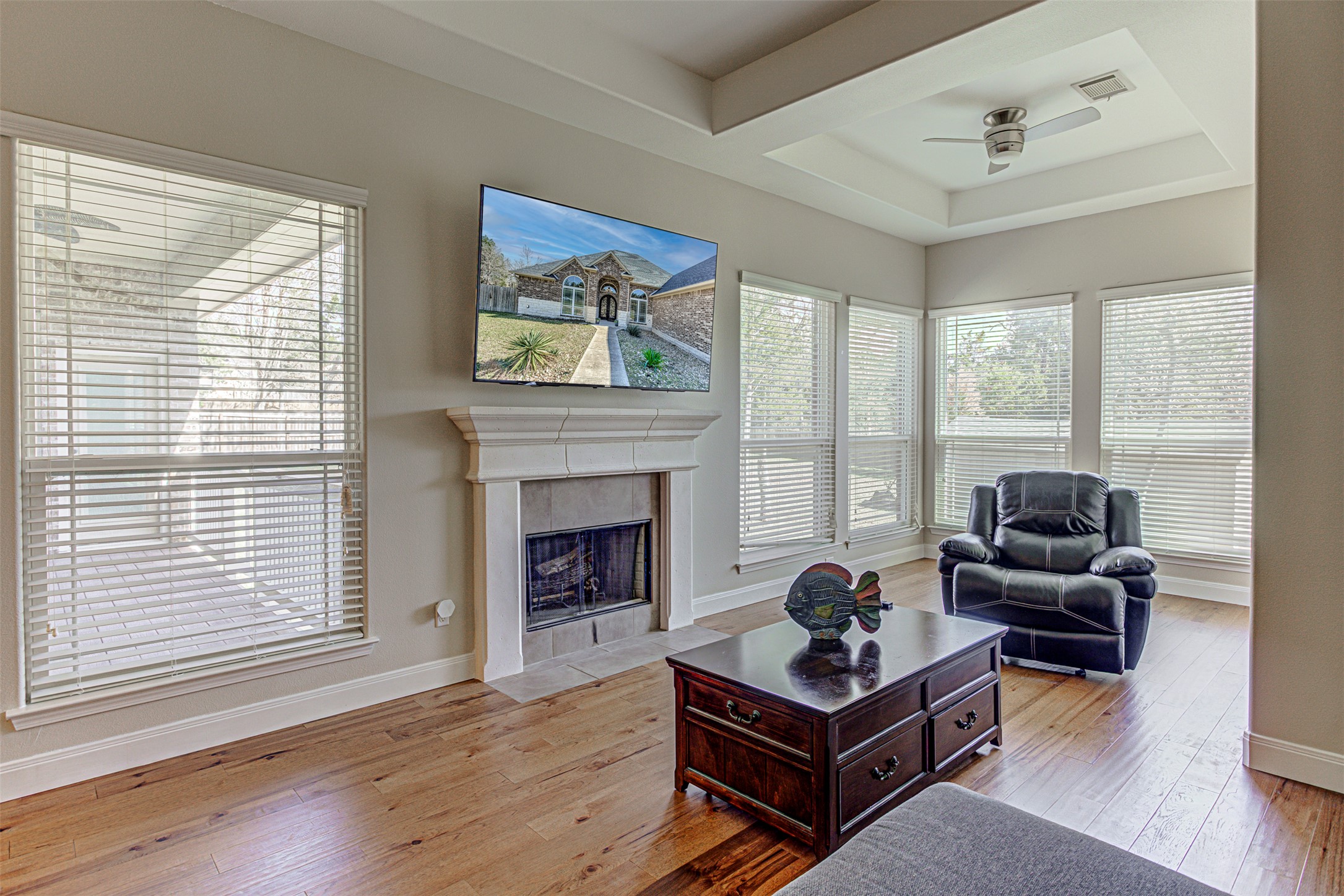 105 Arbors Circle Elgin, TX 78621 - Photo 21 of 40 Living area with light wood-type flooring, a ceiling fan, a raised ceiling, and a tile fireplace