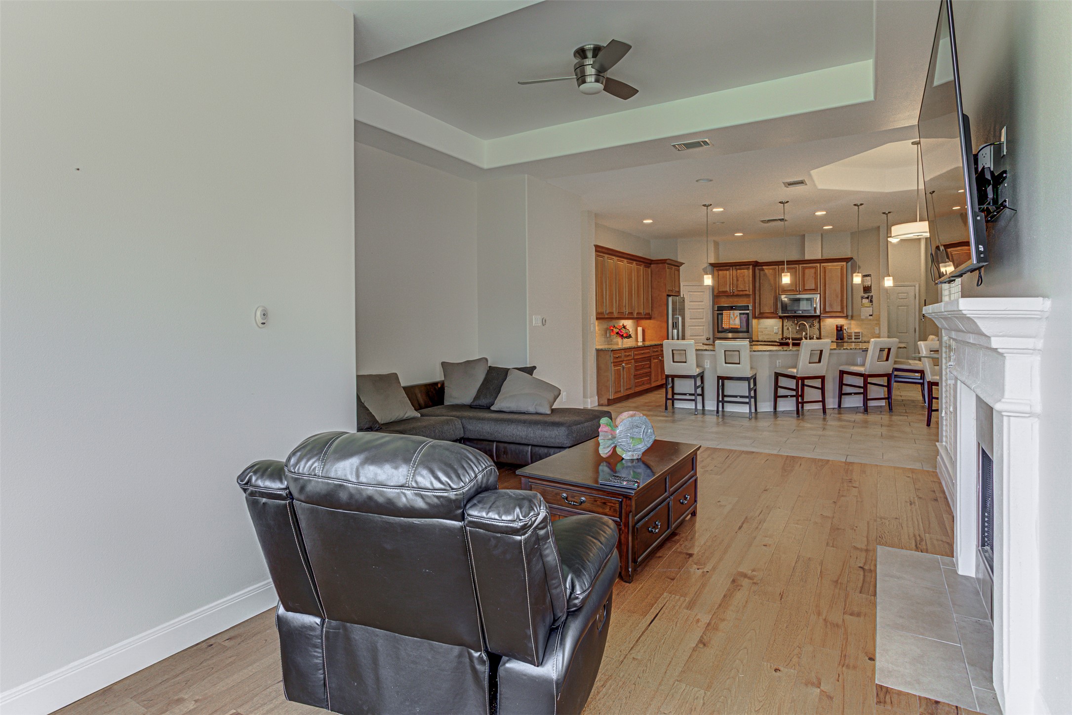 105 Arbors Circle Elgin, TX 78621 - Photo 22 of 40 Living area with a tray ceiling, a fireplace with flush hearth, light wood-type flooring, and a ceiling fan