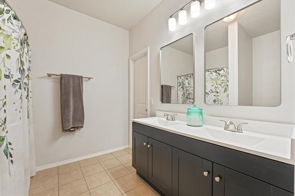 3801 Surf Street Denton, TX 76208 - Photo 21 of 29 Full bathroom featuring double vanity, light tile patterned floors, and curtained shower